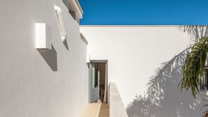 A narrow, sunlit corridor with a door leading to a room, white walls, and a palm tree casting a shadow. - Dimora Biancarancio - Epoca Collection (Ostuni)