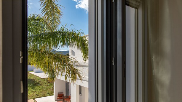 A view through a window of a modern building with a patio area, outdoor furniture, and a palm tree. - Dimora Biancarancio - Epoca Collection (Ostuni)