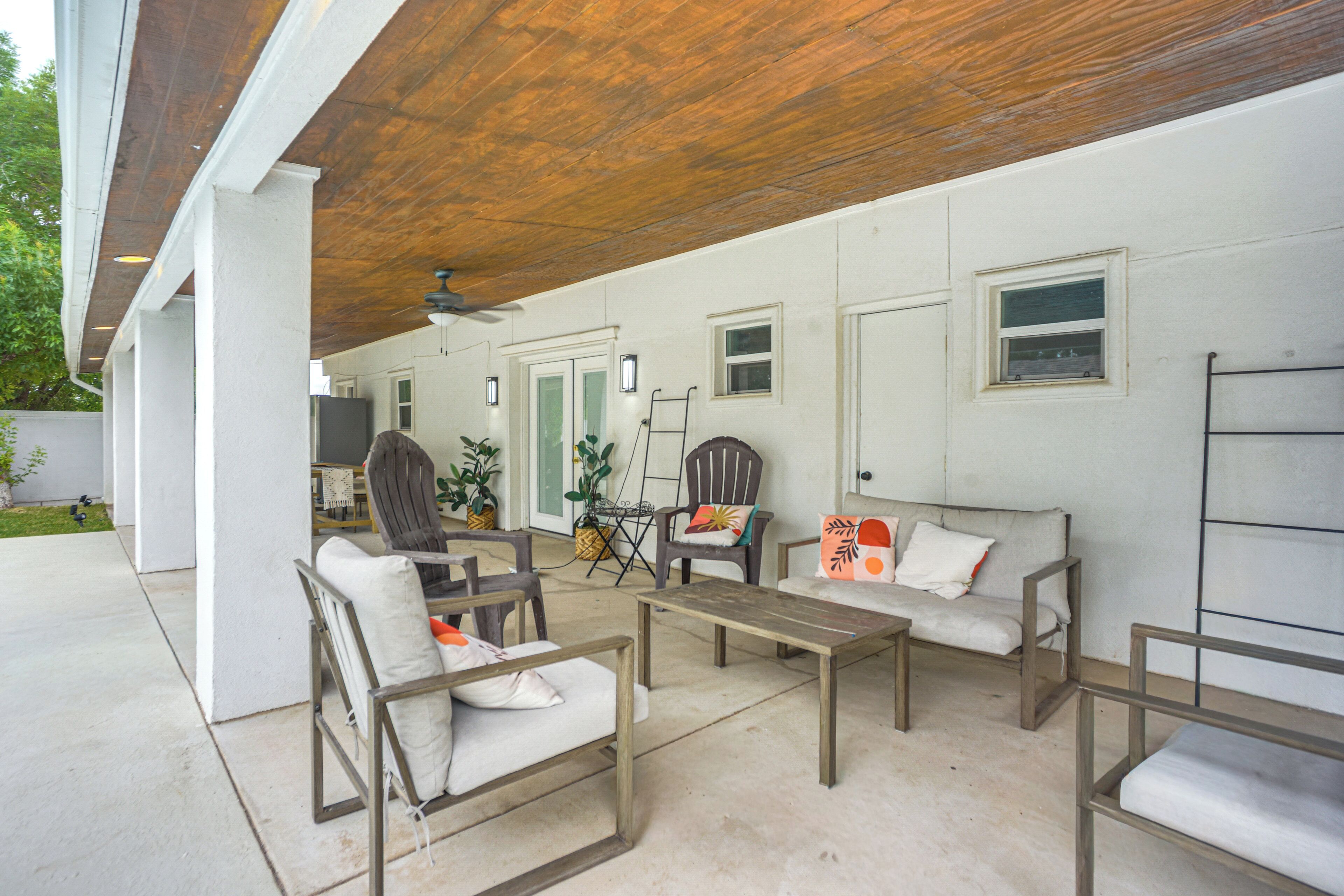 Un espace extérieur aménagé en terrasse, doté d’un plafond en bois, de murs blancs et d’un coin salon comprenant des chaises et un canapé.