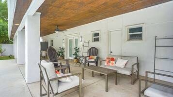 Un espace extérieur aménagé en terrasse, doté d’un plafond en bois, de murs blancs et d’un coin salon comprenant des chaises et un canapé.