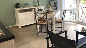 A modern living room with a dining area, featuring a flat-screen TV, a wicker lamp, and a view through a large window. - Cosy park near Grande Plage awarded 3-star label (Carnac)