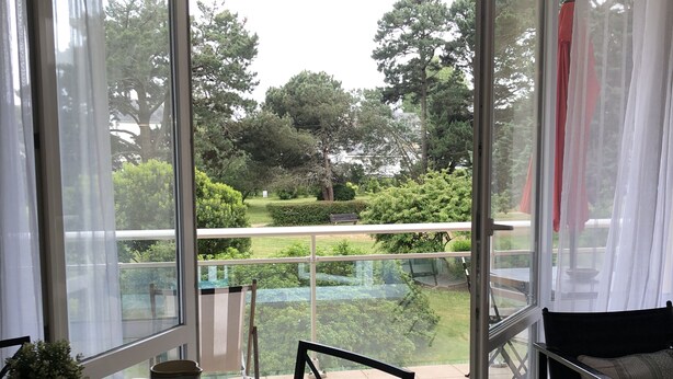 A dining area with a table set for two, a potted plant, and a view of a garden through large glass doors. - Cosy park near Grande Plage awarded 3-star label (Carnac)