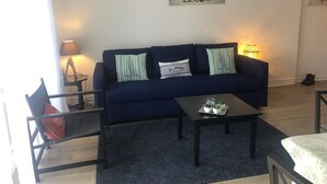 A living room with a dark blue sofa, two striped pillows, a small coffee table with plants, a lamp, and a painting on the wall. - Cosy park near Grande Plage awarded 3-star label (Carnac)
