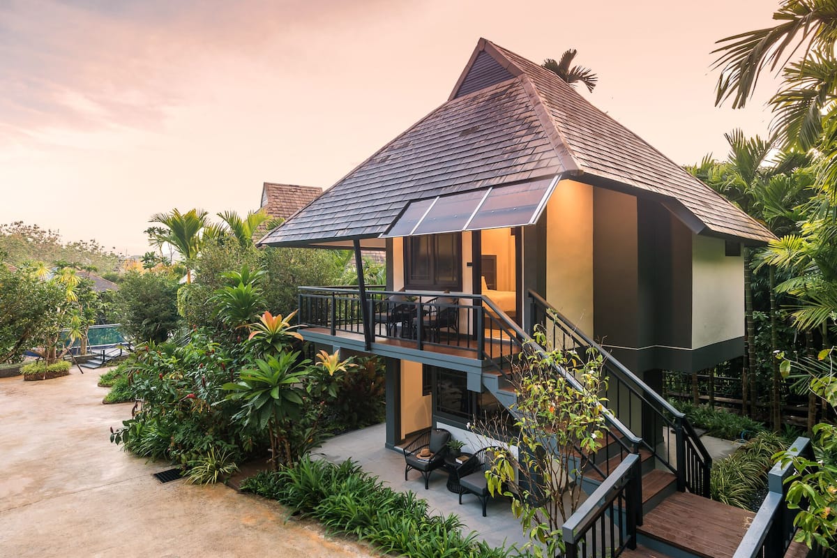A modern house with a balcony, surrounded by lush greenery.