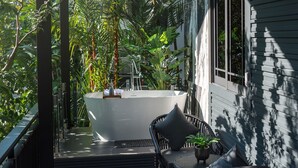 A modern outdoor bathroom with a freestanding bathtub, surrounded by lush greenery and a seating area with a table and chairs. - Loy Chalet (Krabi)