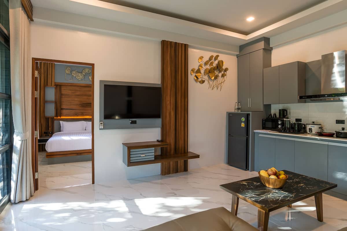 A modern hotel room with a bed, TV, wooden decor, kitchen area, and a marble floor.