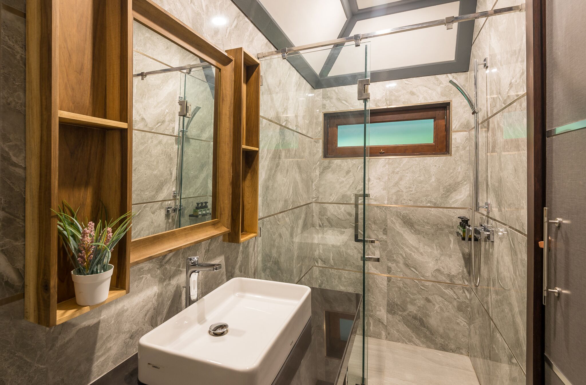 A modern bathroom with a glass-enclosed shower, a large mirror, and a potted plant.