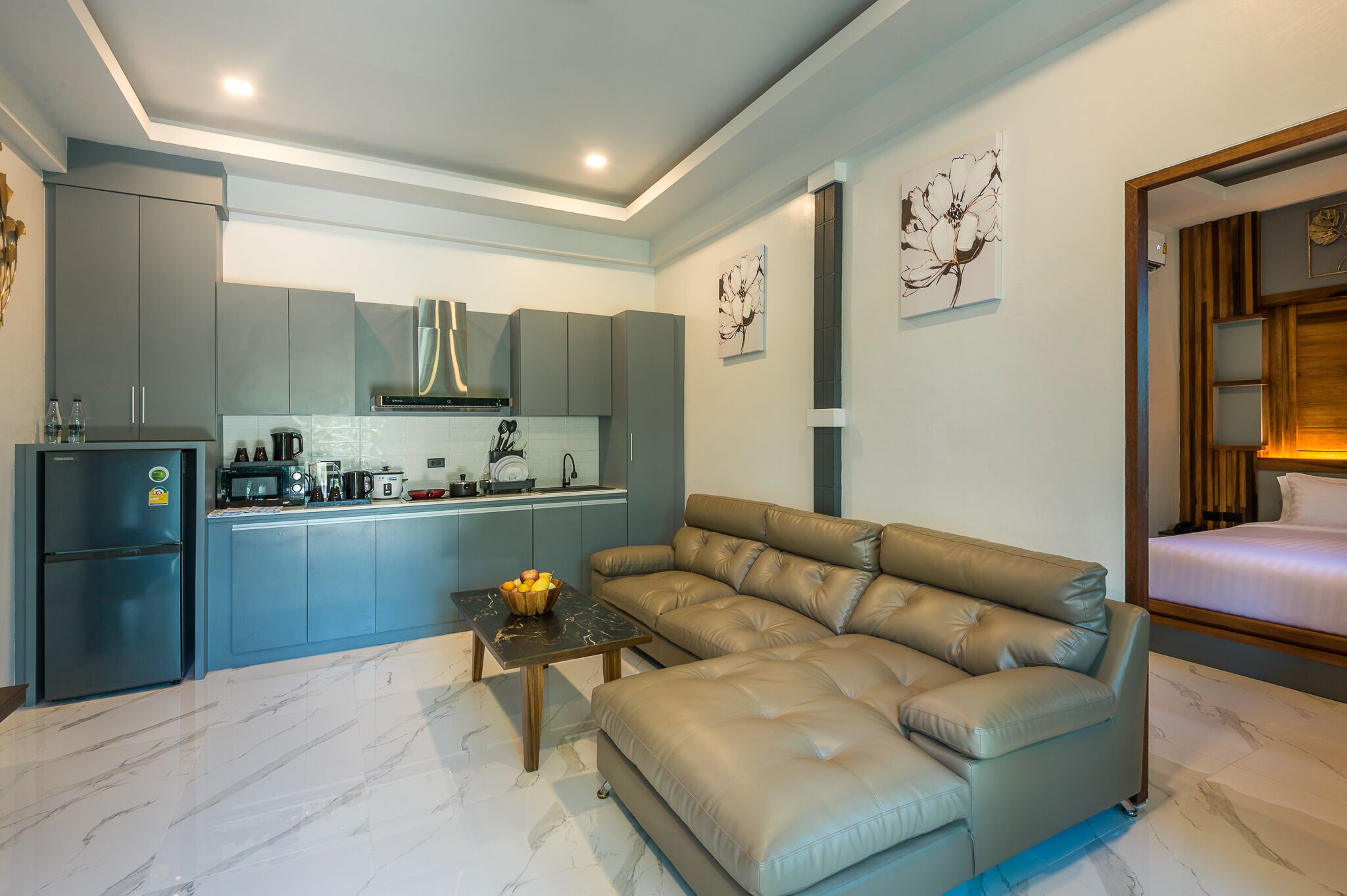 A modern kitchen with grey cabinets, a black refrigerator, and a dining area with a beige sofa and a small table.