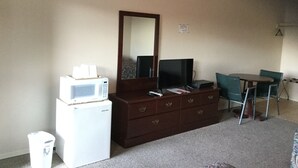 A hotel room with a kitchenette, a dresser, a mirror, a television, and a dining table with chairs. - Americana Inn (Sierra Blanca)