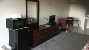 A compact hotel room with a dark wooden dresser, a small black TV, a red chair, and a round table. - Americana Inn (Sierra Blanca)