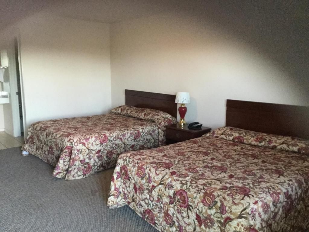 A hotel room with two beds, a nightstand, and a lamp.