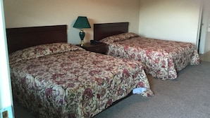 A hotel room with two beds, each with floral bedding, a nightstand with a lamp, and a plain wall. - Americana Inn (Sierra Blanca)