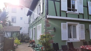 A courtyard with a green building, white shutters, and outdoor seating. - Le chat Vert, bright and modern 2-room apartment (Strasbourg)