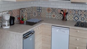 A compact kitchen with wooden cabinets, a microwave, a dishwasher, and a coffee maker. - Le chat Vert, bright and modern 2-room apartment (Strasbourg)