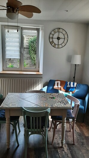 Cozy living space with a dining area featuring a table for two, a sofa, and a wall clock.