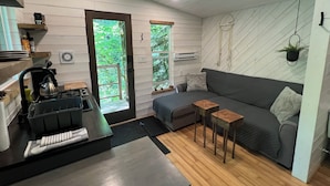 A modern living space with a kitchen area, a grey sofa, and a small wooden table. - Squamish Tree House (Brackendale)