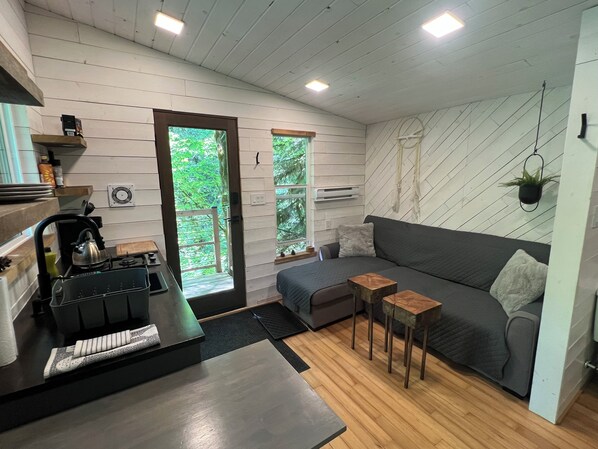 A modern living space with a kitchen area, a grey sofa, and a small wooden table. - Squamish Tree House (Brackendale)