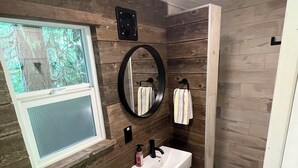 A compact bathroom with a window, a sink, a toilet, and a shower. - Squamish Tree House (Brackendale)