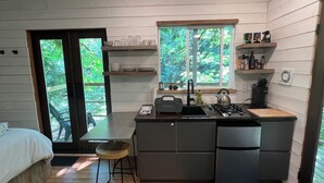 A compact kitchen with a sink, stove, and a window overlooking greenery. - Squamish Tree House (Brackendale)