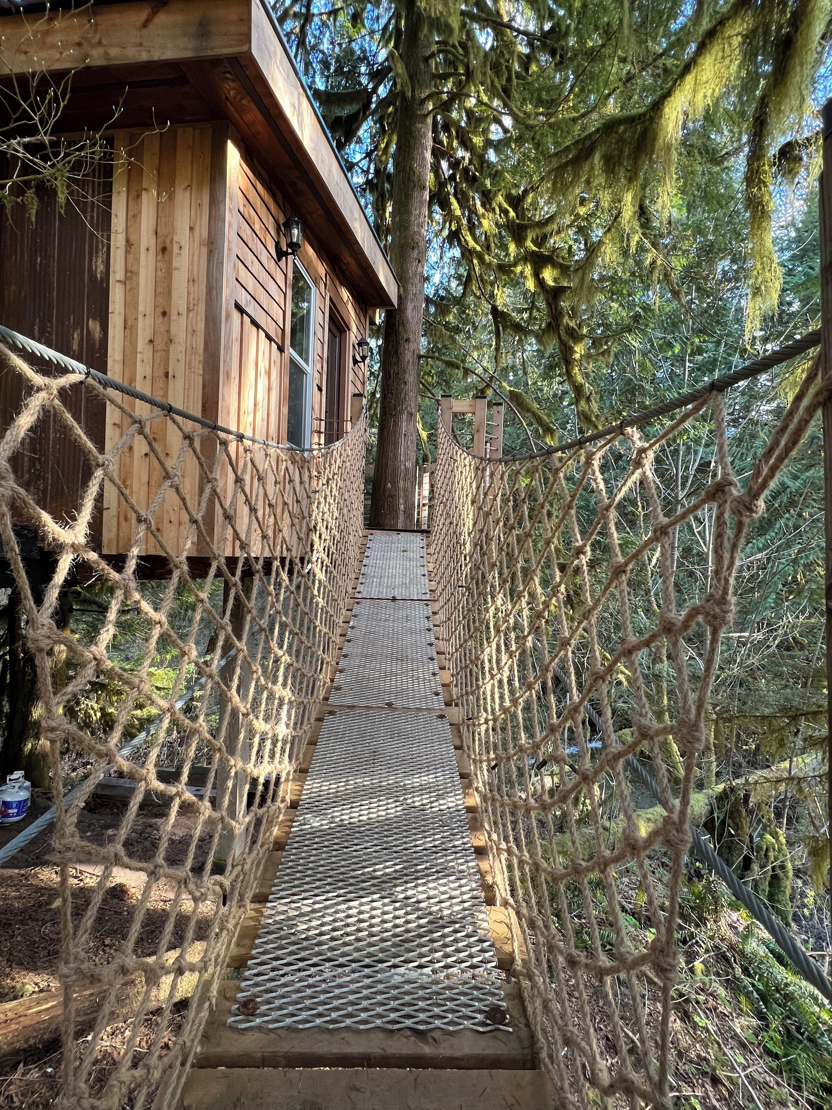 A wooden cabin with a rope bridge leading to a wooden deck.
