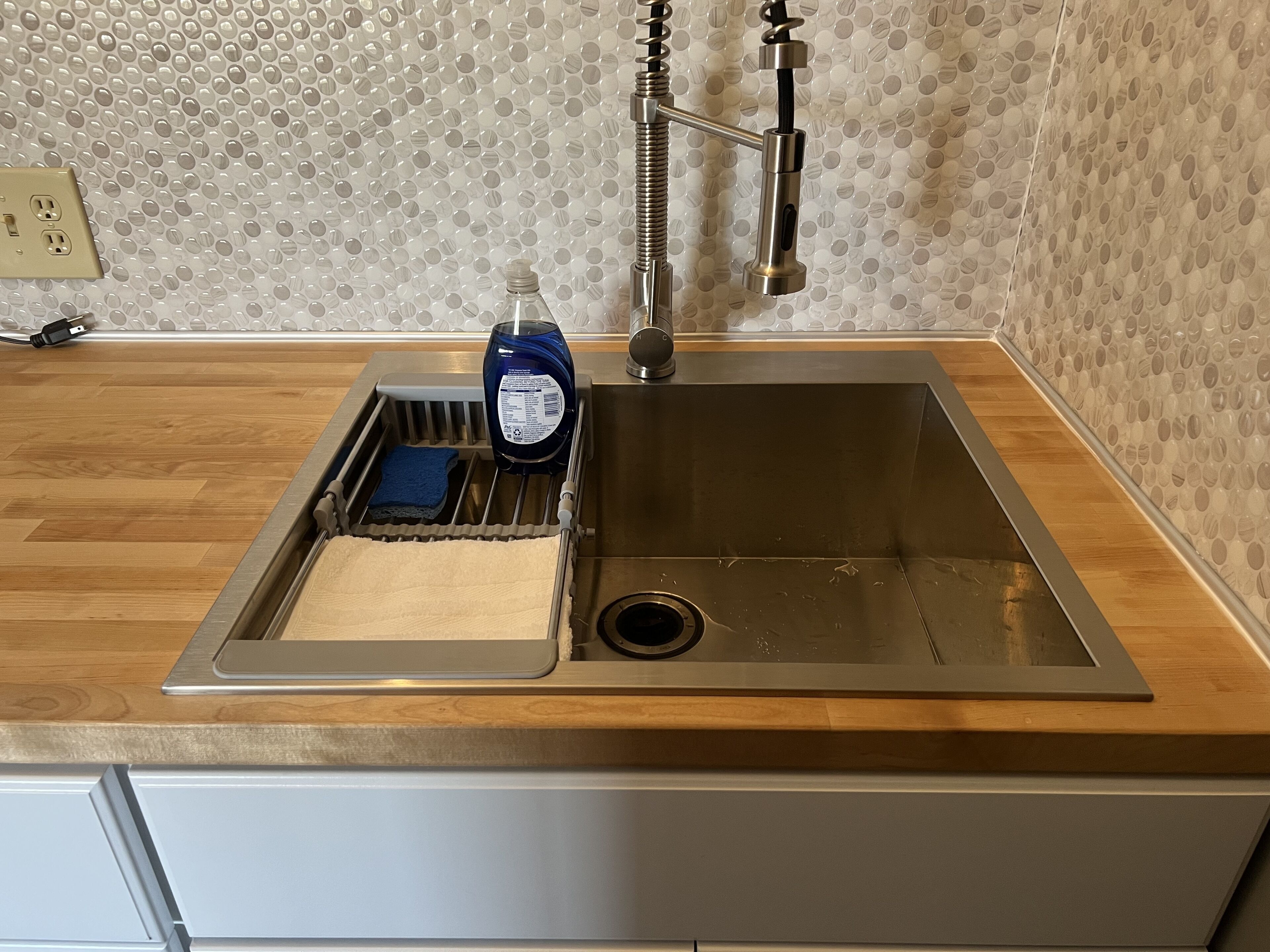 A kitchen sink with a soap dispenser, a sponge, and a towel.