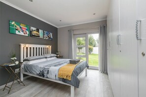 Une chambre à coucher moderne avec un lit, une petite table de chevet, une grande fenêtre et des œuvres d’art accrochées au mur.