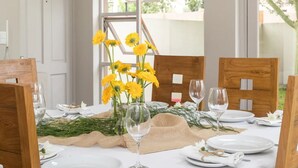 Une table à manger dressée avec de l’argenterie blanche, des verres et un centre de table composé de fleurs jaunes.