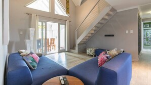 Un salon spacieux avec un canapé bleu, une table basse en bois et un escalier menant à l’étage supérieur.