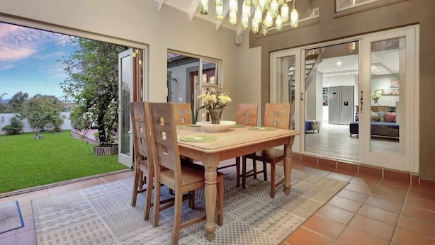 Un coin repas avec une table et des chaises en bois, un lustre et une vue sur un jardin, visible à travers des portes vitrées.
