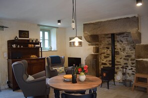 Ein gemütliches Wohnzimmer mit Kamin aus Stein, einem runden Holztisch mit Blumenvase und einem Fernseher auf einer Holzkommode.