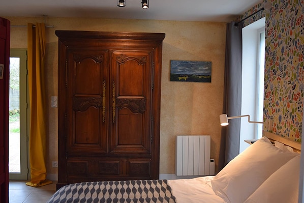 Un dormitorio con un armario grande de madera, una cama con manta a cuadros, un radiador y una ventana con cortina.