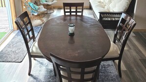 Een eetgedeelte met een ronde tafel, vier stoelen, een kaars en uitzicht op een voertuig door grote ramen.