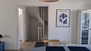A room with a staircase, a framed artwork on the wall, a dining area with a table and chairs, and a cabinet with glass doors. - Between Nausicaa and Wimereux, bright and spacious house, rated 3*. (Boulogne-sur-Mer)