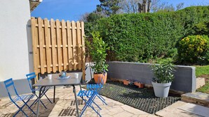 A patio with a table and blue chairs, surrounded by potted plants and a wooden fence. - Between Nausicaa and Wimereux, bright and spacious house, rated 3*. (Boulogne-sur-Mer)
