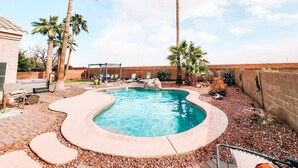 Un jardin avec une piscine, des palmiers et un espace barbecue.