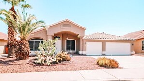 Une maison d’habitation à la façade beige, dotée d’un garage et d’un jardin aménagé avec un palmier et des cactus.