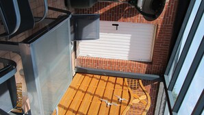 Ein Balkon mit Holzboden, Metallgeländer und Blick auf eine Ziegelwand und eine Garagentür.