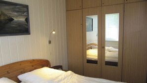 Ein Schlafzimmer mit einem hölzernen Bett, einem Nachttisch, einer Wandlampe und einem Kleiderschrank mit Spiegelüren.