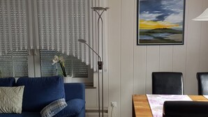 Una sala de estar con un sofá azul, una lámpara de pie, una mesa con sillas y un cuadro en la pared.