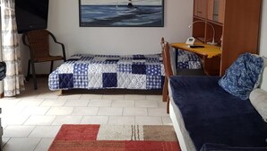 Una habitación pequeña con una cama, una silla, un escritorio, un televisor y un cuadro de un faro en la pared.