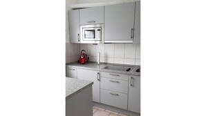 Una cocina con armarios grises, microondas, tetera y lavamanos.
