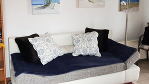 Un sofá blanco con funda azul oscuro y almohadones estampados, frente a una pared blanca con tres cuadros con motivos marinos.