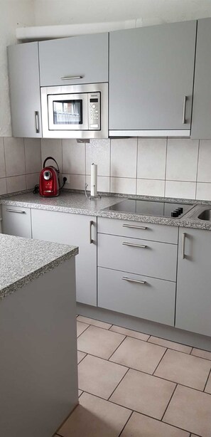 A kitchen with grey cabinets, a microwave, a kettle, and a sink.