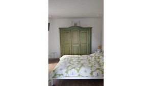 Um quarto com um guarda-roupa verde, uma cama com colcha floral e uma pequena mesa de cabeceira.