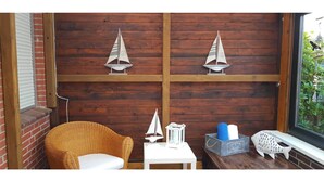 Um canto aconchegante com uma cadeira de vime, uma mesa pequena com um candeeiro, e objetos decorativos como um modelo de barco à vela e um peixe.