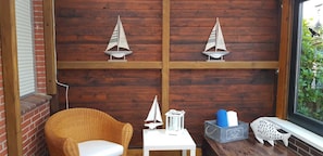 A cozy corner with a wicker chair, a small table with a lantern, and decorative items including a sailboat and a fish model.