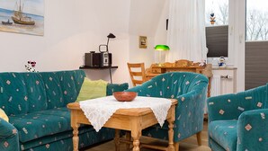 Ein gemütliches Wohnzimmer mit türkisfarbenen Möbeln mit Muster, einem Holztisch mit einer Schale, einem Radio und einer Lampe.