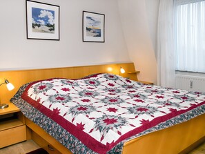 Quarto com cama, mesas de cabeceira, um criado-mudo e duas fotografias emolduradas na parede.