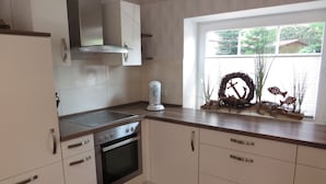 Een moderne keuken met witte kastjes, roestvrijstalen apparatuur en een raam met uitzicht op groen.