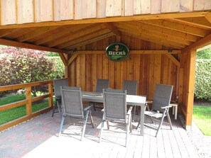 Um deck de madeira ao ar livre com uma mesa e cadeiras, um letreiro da cerveja Beck's e um jardim ao fundo.